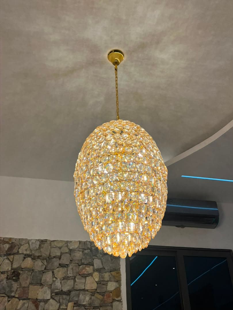 Crystal chandelier installed by KENVO in a high-ceilinged room with a stone feature wall