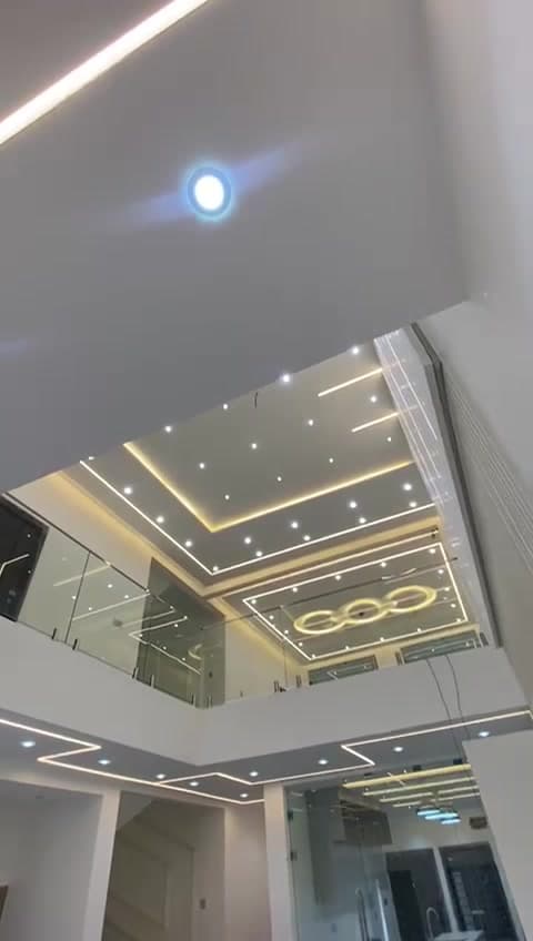 Double-height interior lit by recessed linear LED profiles and cove lighting installed by KENVO